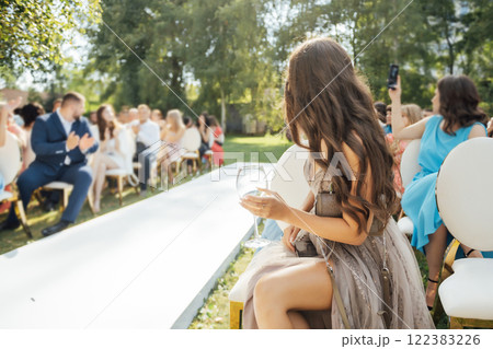 Invited guest girl in sexy dress with long slit sits in front row with champagne at wedding ceremony 122383226