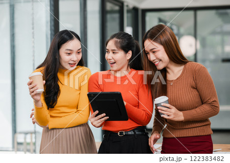 Three young women in a modern office setting, sharing a tablet and enjoying coffee, expressing excitement and joy. Three young women in a modern office setting, sharing a tablet and enjoying coffee, expressing excitement and joy. 122383482