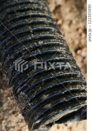 A CloseUp View of a Black Ribbed Pipe Resting on a Dirty and Grimy Surface Below A CloseUp View of a Black Ribbed Pipe Resting on a Dirty and Grimy Surface Below 122383890