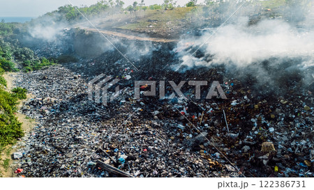 Burning landfill emitting smoke, highlighting environmental pollution and waste management challenges in landscape 122386731
