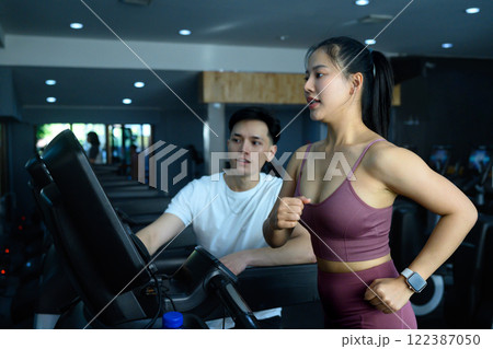 Young woman jogging on treadmill while her trainer monitors her progress and provides guidance 122387050