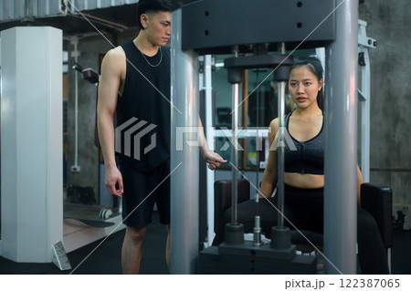 Female athlete exercising on a leg press machine under the supervision of her trainer Female athlete exercising on a leg press machine under the supervision of her trainer 122387065