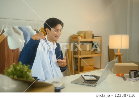 Online fashion seller presenting a product in front of his laptop Online fashion seller presenting a product in front of his laptop 122387110