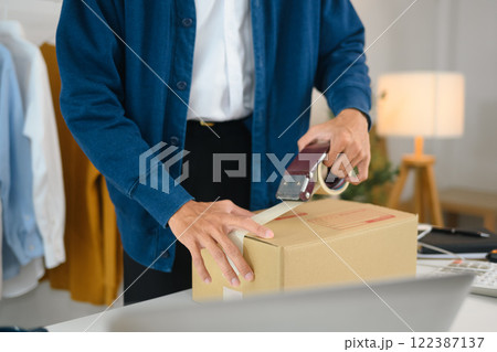 Business owner taping a shipping box preparing for delivery to costumer Business owner taping a shipping box preparing for delivery to costumer 122387137