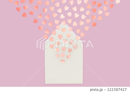 Creative minimalist composition of cream letter envelope spilling heart-shaped confetti, set against a pink background, symbolizing love and warmth. 122387427