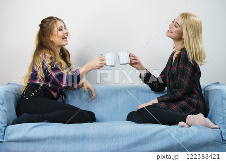 Female friends sitting on sofa having fun Female friends sitting on sofa having fun 122388421