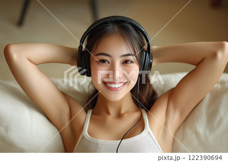 Happy Asian woman at headphones listening music relax on sofa. AI-generated item 122390694