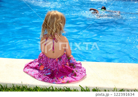 Little blond girl sitting rear back swimming pool 122391634
