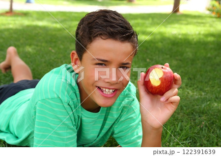 boy teenager eating red apple on garden grass 122391639