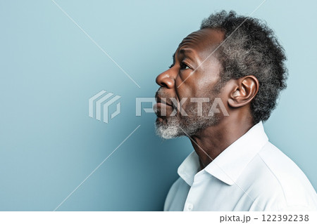 Middle-aged Black man in white shirt looking thoughtfully while posed against a blue background 122392238