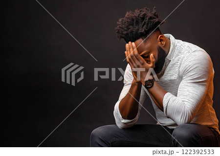 Black man reflecting in a dark room, conveying deep thought and emotion 122392533