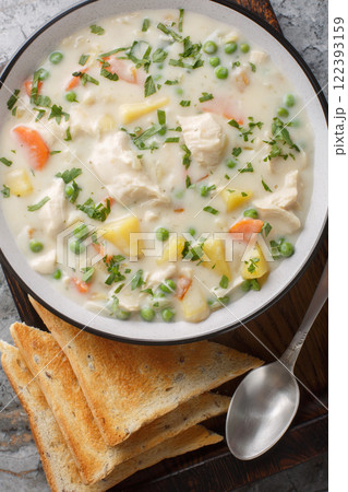 Homemade Chicken Pot Pie Soup with shredded chicken, vegetables, and a rich and creamy broth closeup on the wooden board. Vertical top view 122393159