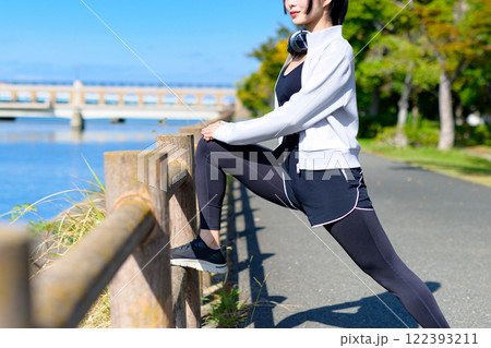 川沿いの柵で脚のストレッチをするかっこいい女性　歩く　ダイエット　散歩　運動　トリミングアップ 122393211