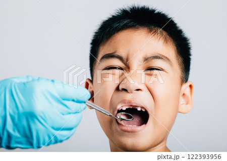 In a dental office a pediatric dentist examines a child's mouth after extraction of a loose milk tooth. Dental instruments aid in examination process. Doctor uses mouth mirror to checking teeth cavity 122393956