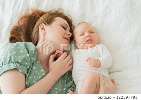 Happy family at home. Mother playing with little toddler child on bed. Mom baby relax playing having fun together. Mother looks at baby with love care. Mom of breast feeding baby rest in living room Happy family at home. Mother playing with little toddler child on bed. Mom baby relax playing having fun together. Mother looks at baby with love care. Mom of breast feeding baby rest in living room 122397793