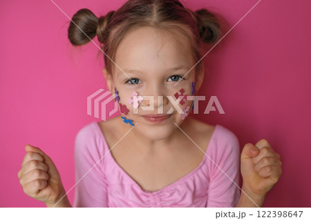 A cheerful girl stands with her fists clenched as a sign of support and solidarity with children with autism spectrum disorder. Pieces of a colored puzzle on a child's face A cheerful girl stands with her fists clenched as a sign of support and solidarity with children with autism spectrum disorder. Pieces of a colored puzzle on a child's face 122398647