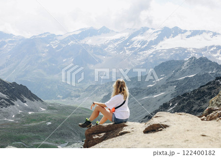A young woman sitting on a mountain peak, taking in the breathtaking view from the summit 122400182