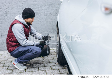 Man changing his car's tire with a wrench, replacing it with winter tires for the season Man changing his car's tire with a wrench, replacing it with winter tires for the season 122400428
