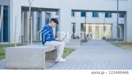Focused student working on laptop outside university building 122400466