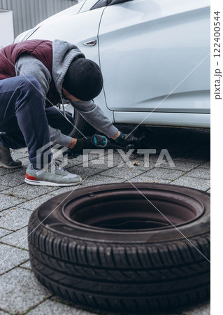 Man changing his car's tire with a wrench, replacing it with winter tires for the season Man changing his car's tire with a wrench, replacing it with winter tires for the season 122400544