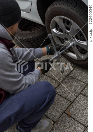 Young man changing a car tire on the road, using a wrench to unscrew the lug nuts Young man changing a car tire on the road, using a wrench to unscrew the lug nuts 122400546