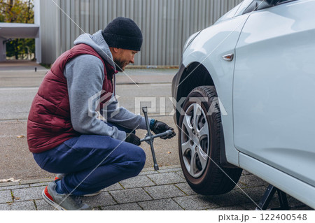 Man changing his car's tire with a wrench, replacing it with winter tires for the season Man changing his car's tire with a wrench, replacing it with winter tires for the season 122400548