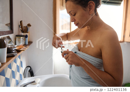 Woman in Bathroom Brushing Teeth Surrounded by Simple Home Environment Woman in Bathroom Brushing Teeth Surrounded by Simple Home Environment 122401136