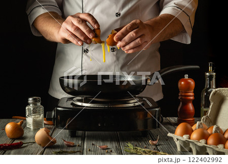 A culinary expert expertly breaks fresh eggs into a sizzling frying pan, surrounded by kitchen tools and ingredients 122402992