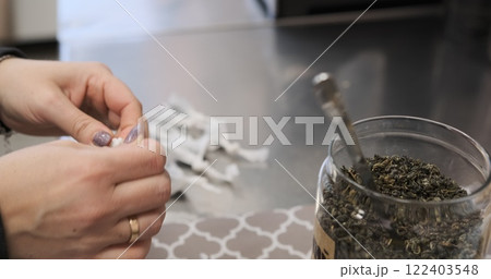 Female hands carefully portion loose tea into individual tea bags for brewing creating neatly packed servings. Close-up of a precise packaging process emphasizing manual craftsmanship. 122403548