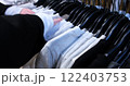 young woman browses through t-shirts on hangers in a clothing store examines each item showcasing the shopping experience variety of styles available perfect for those trendy wardrobe additions 122403753