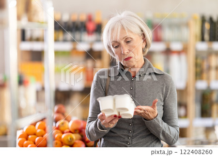 Elderly woman chooses tasty yogurt to buy in the grocery department section of store Elderly woman chooses tasty yogurt to buy in the grocery department section of store 122408260