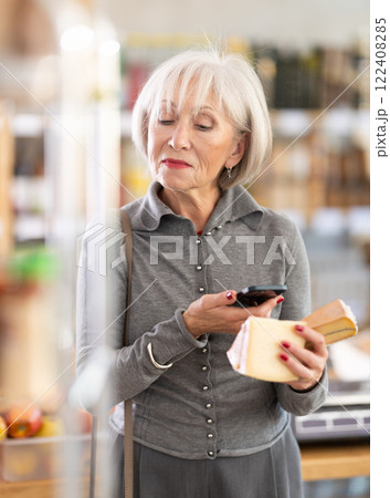 Mature female buyer scans QR code on cheese label in grocery store Mature female buyer scans QR code on cheese label in grocery store 122408285