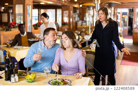 Resentful wife scolding her husband spending time with another woman at dinner Resentful wife scolding her husband spending time with another woman at dinner 122408589