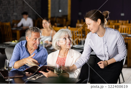 Mature man and woman reads menu and makes order to waitress 122408619