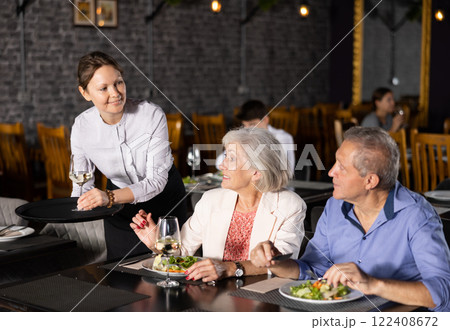 Female waiter serving wine to elderly couple in restaurant 122408672