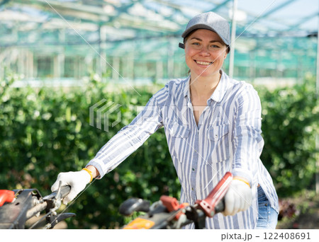 Positive female horticulturist pushing hand tractor in greenhouse Positive female horticulturist pushing hand tractor in greenhouse 122408691