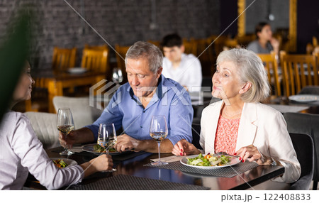 Elderly couple with adult woman having dinner in restaurant Elderly couple with adult woman having dinner in restaurant 122408833