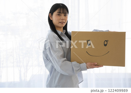 段ボール箱に笑顔のイラストを書いた箱を持つ女性 122409989
