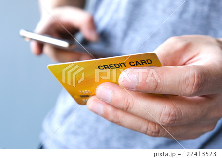 Young man sat in the living room on the sofa holding his credit card. Young man sat in the living room on the sofa holding his credit card. 122413523