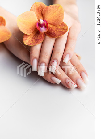 Woman showing stylish white nails with orange orchid decoration Woman showing stylish white nails with orange orchid decoration 122413566