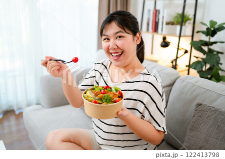 Beautiful plump woman holding a salad bowl and eating a salad in the bowl. 122413798