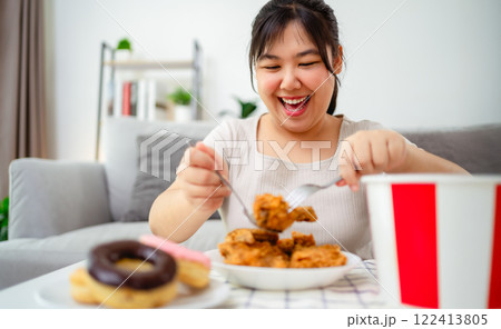 A woman is happily eating fried chicken and donuts on a plate. Fast food, Unhealthy food concept. 122413805