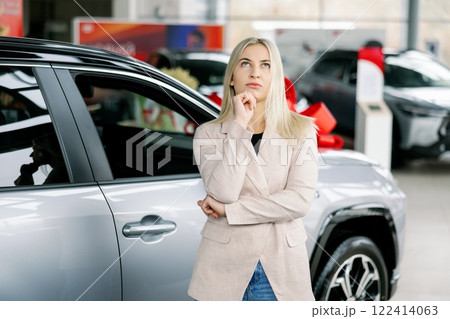 Thoughtful businesswoman choosing new car in dealership showroom 122414063