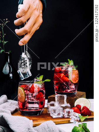 Refreshing summer drink with strawberry slices, lime, and mint leaf in glasses , hand put ice on dark background beverage soda Refreshing summer drink with strawberry slices, lime, and mint leaf in glasses , hand put ice on dark background beverage soda 122417192