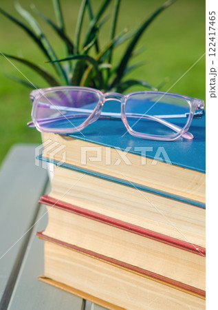 Glasses on stacked colorful books with a potted plant on a wooden table. High quality photo Glasses on stacked colorful books with a potted plant on a wooden table. High quality photo 122417465