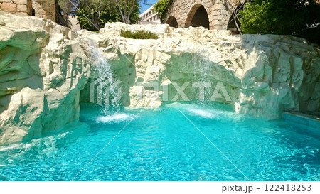 Luxurious hotel pool area with natural rock formations and lush landscaping in bright sunlight 122418253