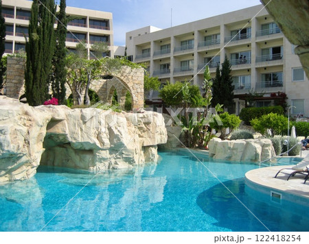 pool invites guests with its clear blue water surrounded by natural rocks and vibrant greenery. Sun loungers offer a perfect spot to relax under the warm sun. 122418254