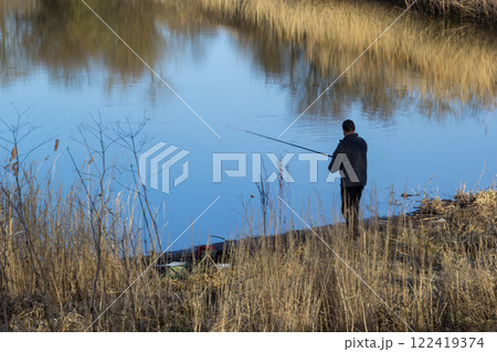 Relaxing day spent fishing by the serene waters of a calm pond surrounded by tall grasses Relaxing day spent fishing by the serene waters of a calm pond surrounded by tall grasses 122419374