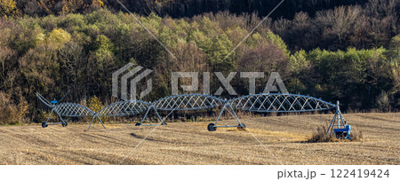 Irrigation system in action over a harvested field surrounded by trees in a rural area during autumn 122419424