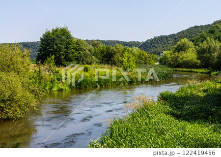 Serene river flows through lush greenery under clear blue sky in a peaceful natural landscape 122419456
